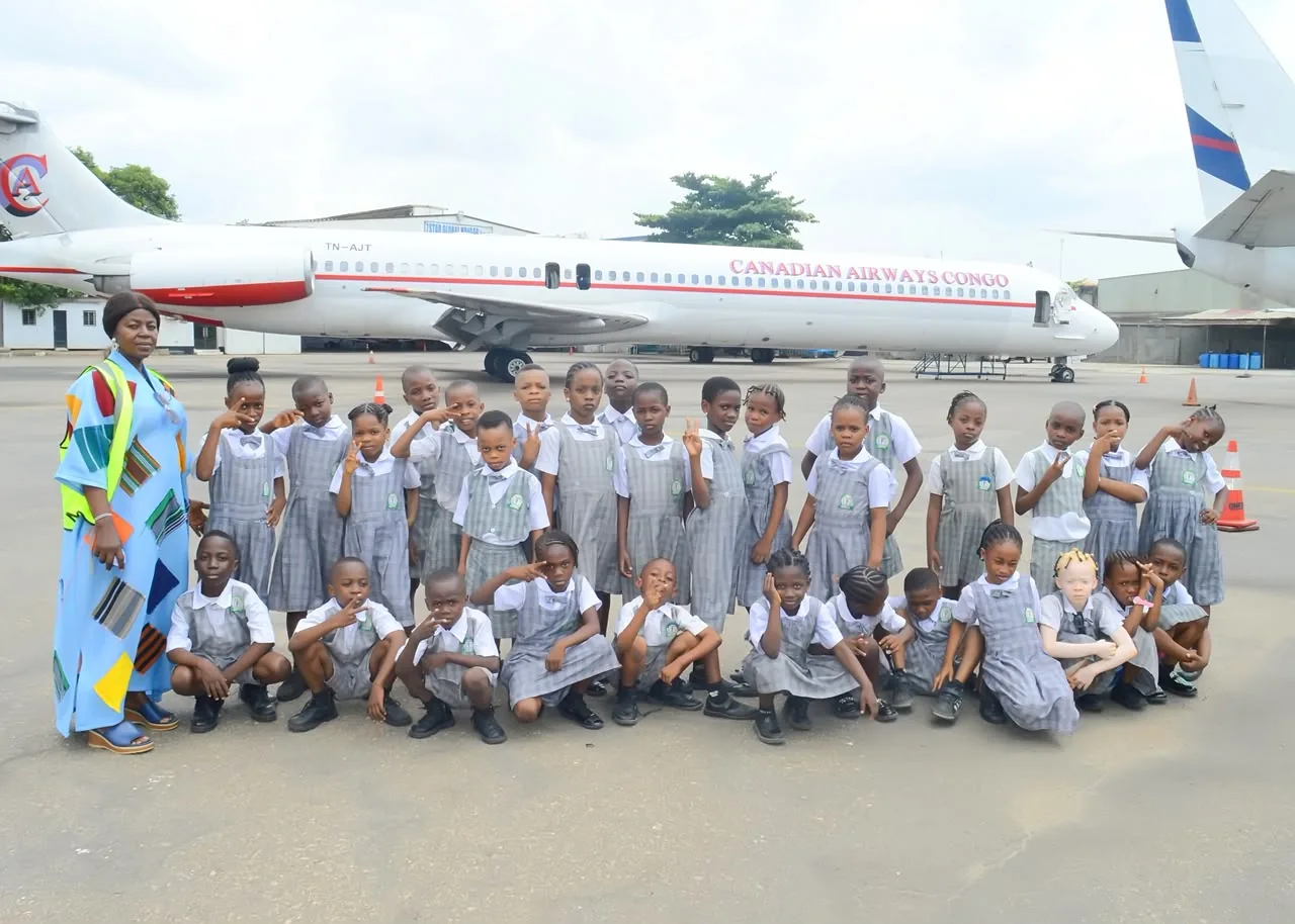 A class of pupils and their teacher posing in front of an aeroplane on the apron
