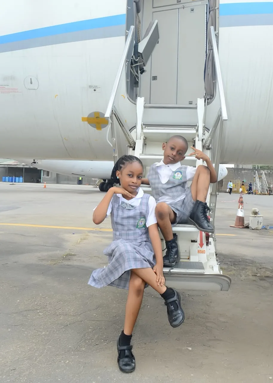 Two pupils in grey check uniform sitting on an aircraft airstair